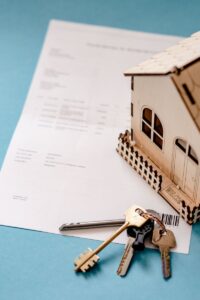 Miniature wooden house with keys and contract symbolizing real estate transactions.