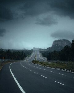A winding highway leads towards a rocky mountain, under a moody, cloudy sky, capturing the essence of adventure and travel.