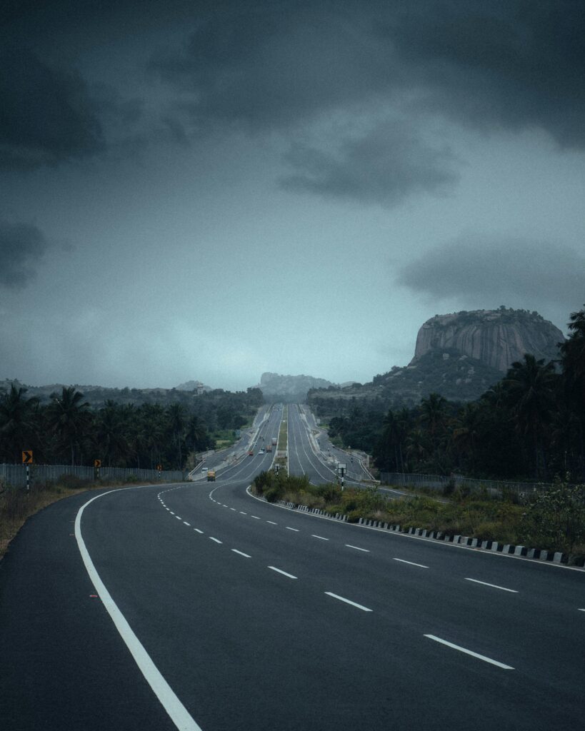 A winding highway leads towards a rocky mountain, under a moody, cloudy sky, capturing the essence of adventure and travel.